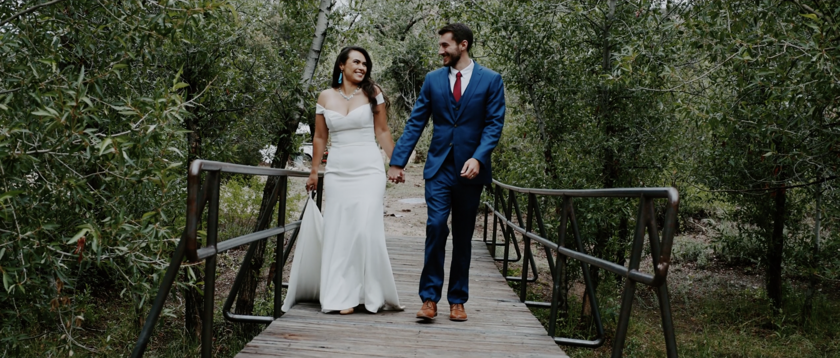 Bride and groom walk hand in hand over a rustic bridge